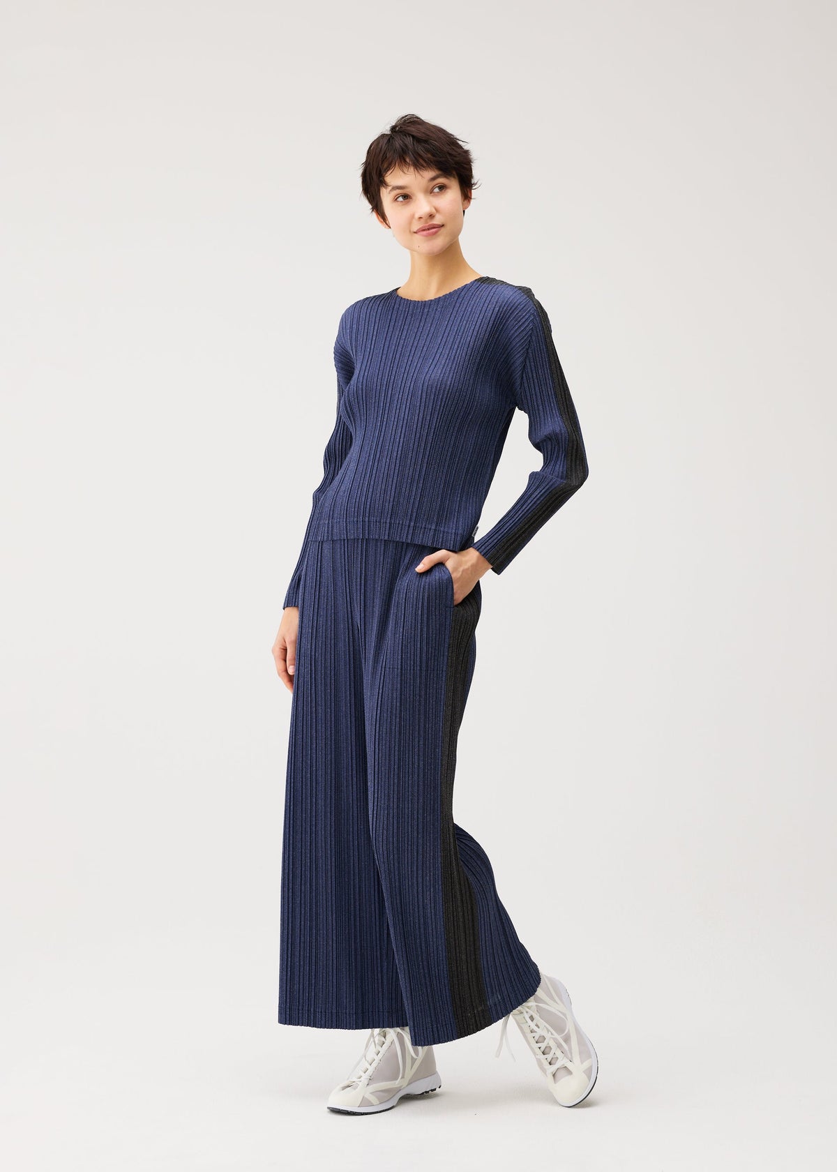 A model wears the PLEATS PLEASE ISSEY MIYAKE COTTON DENIM cotton-denim-trousers-dark-green.