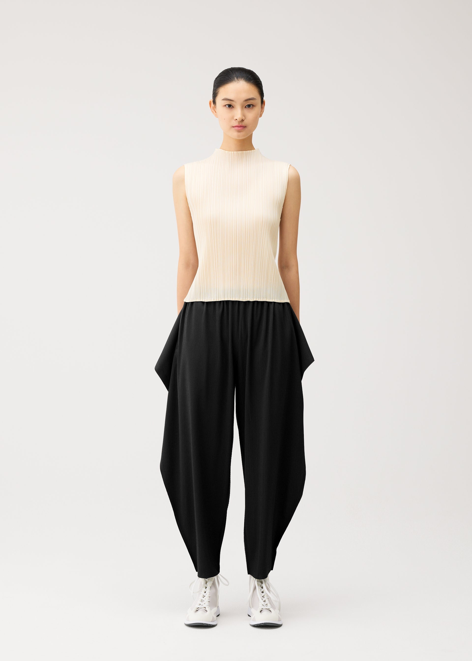 A model wears the PLEATS PLEASE ISSEY MIYAKE A-POC BOTTOMS a-poc-bottoms-side-drape-trousers-black.