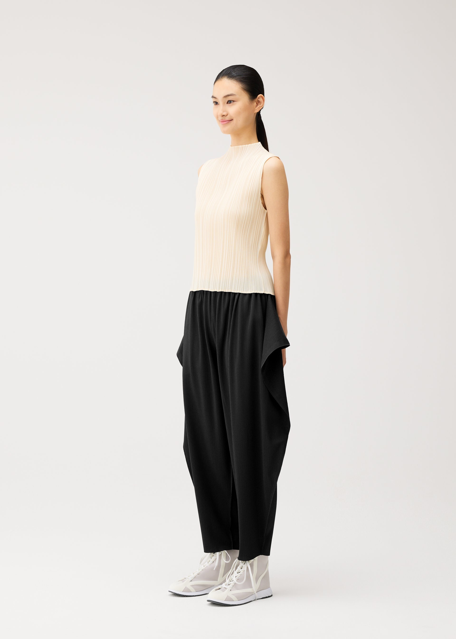 A model wears the PLEATS PLEASE ISSEY MIYAKE A-POC BOTTOMS a-poc-bottoms-side-drape-trousers-black.