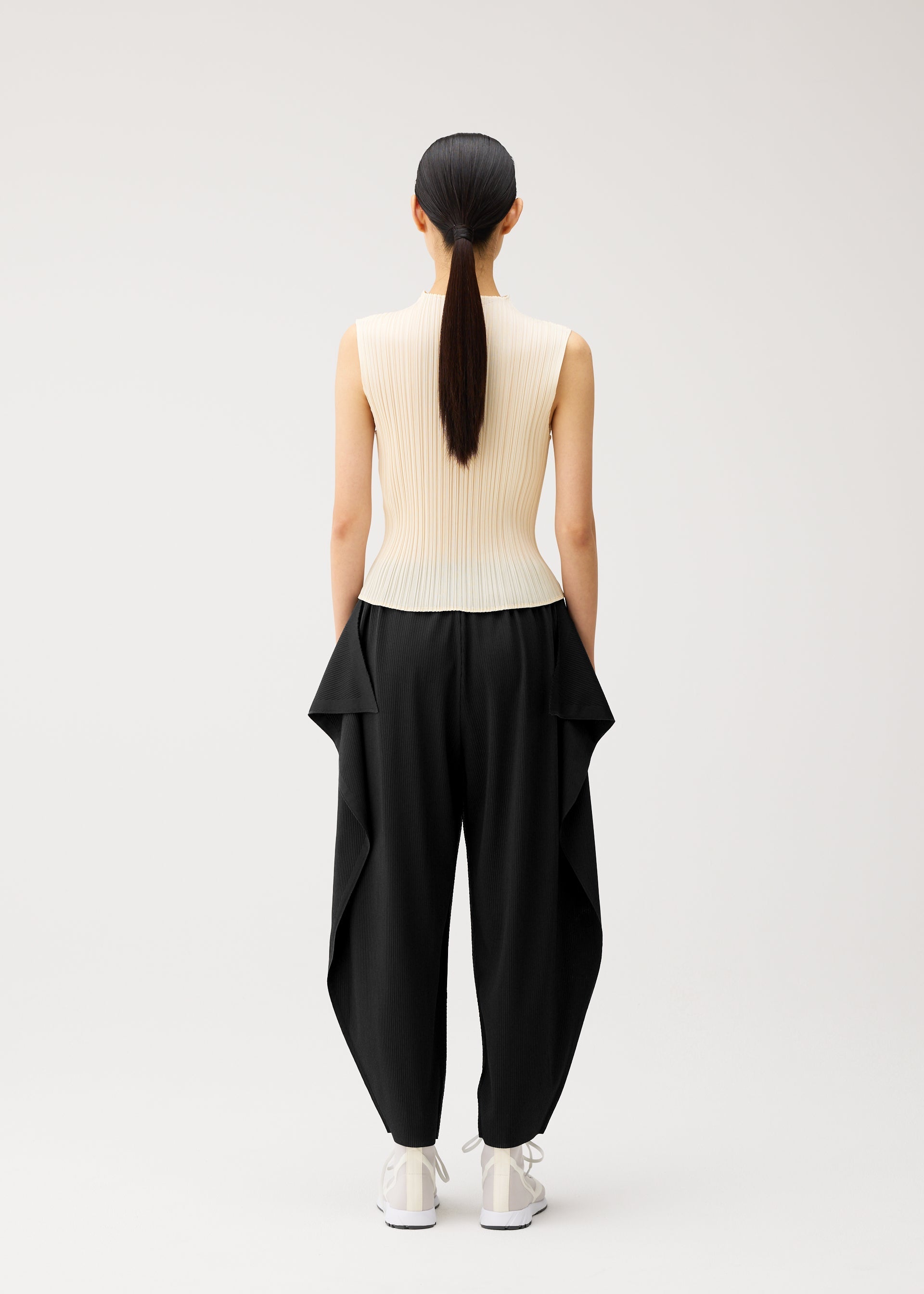 A model wears the PLEATS PLEASE ISSEY MIYAKE A-POC BOTTOMS a-poc-bottoms-side-drape-trousers-black.