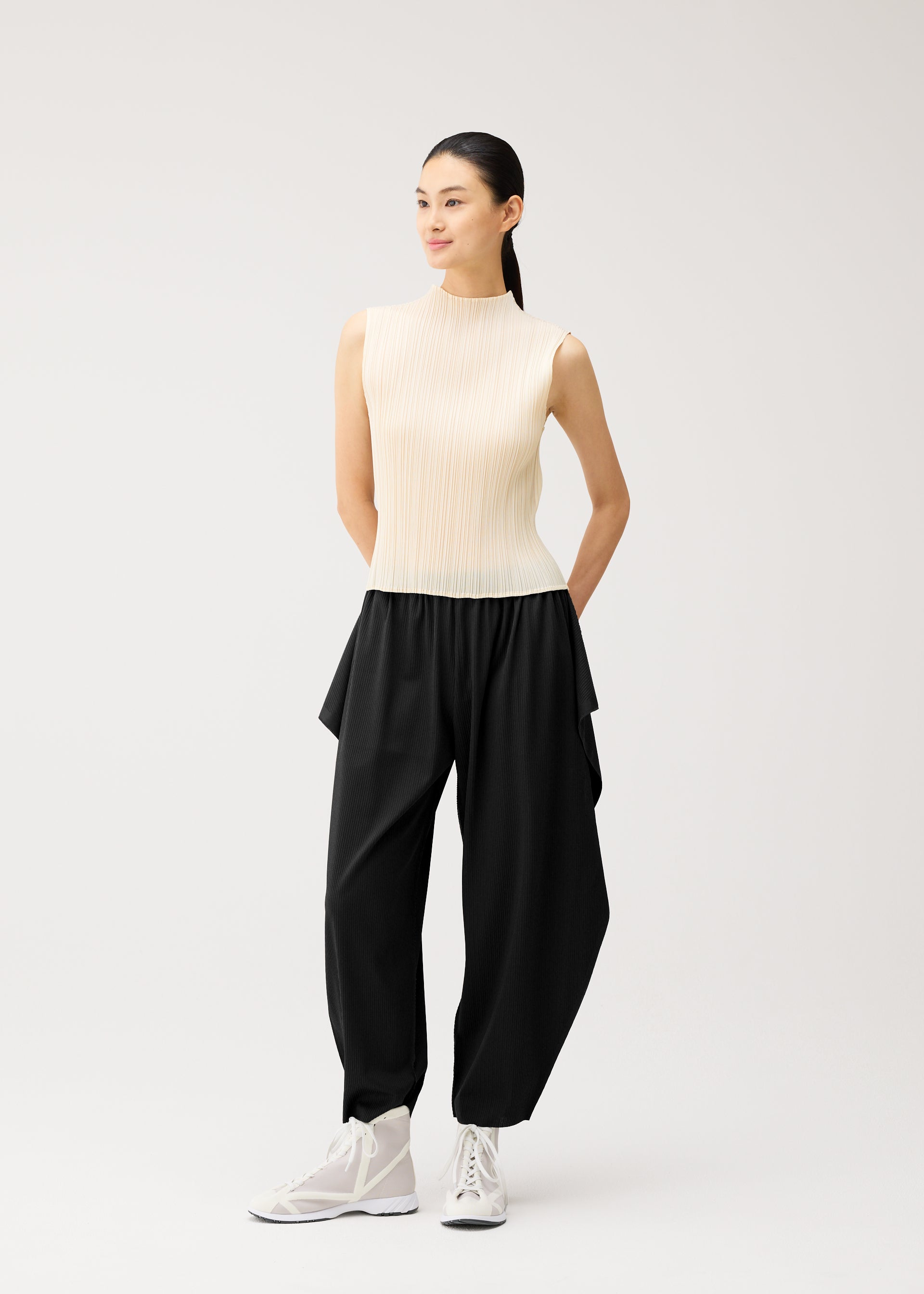 A model wears the PLEATS PLEASE ISSEY MIYAKE A-POC BOTTOMS a-poc-bottoms-side-drape-trousers-black.