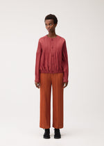 A model wears the PLEATS PLEASE ISSEY MIYAKE SMOOTH COAT smooth-coat-coat-terracotta.