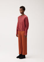 A model wears the PLEATS PLEASE ISSEY MIYAKE SMOOTH COAT smooth-coat-coat-terracotta.