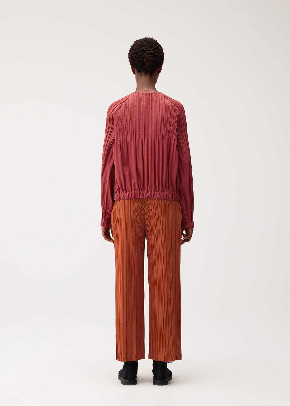 A model wears the PLEATS PLEASE ISSEY MIYAKE SMOOTH COAT smooth-coat-coat-terracotta.