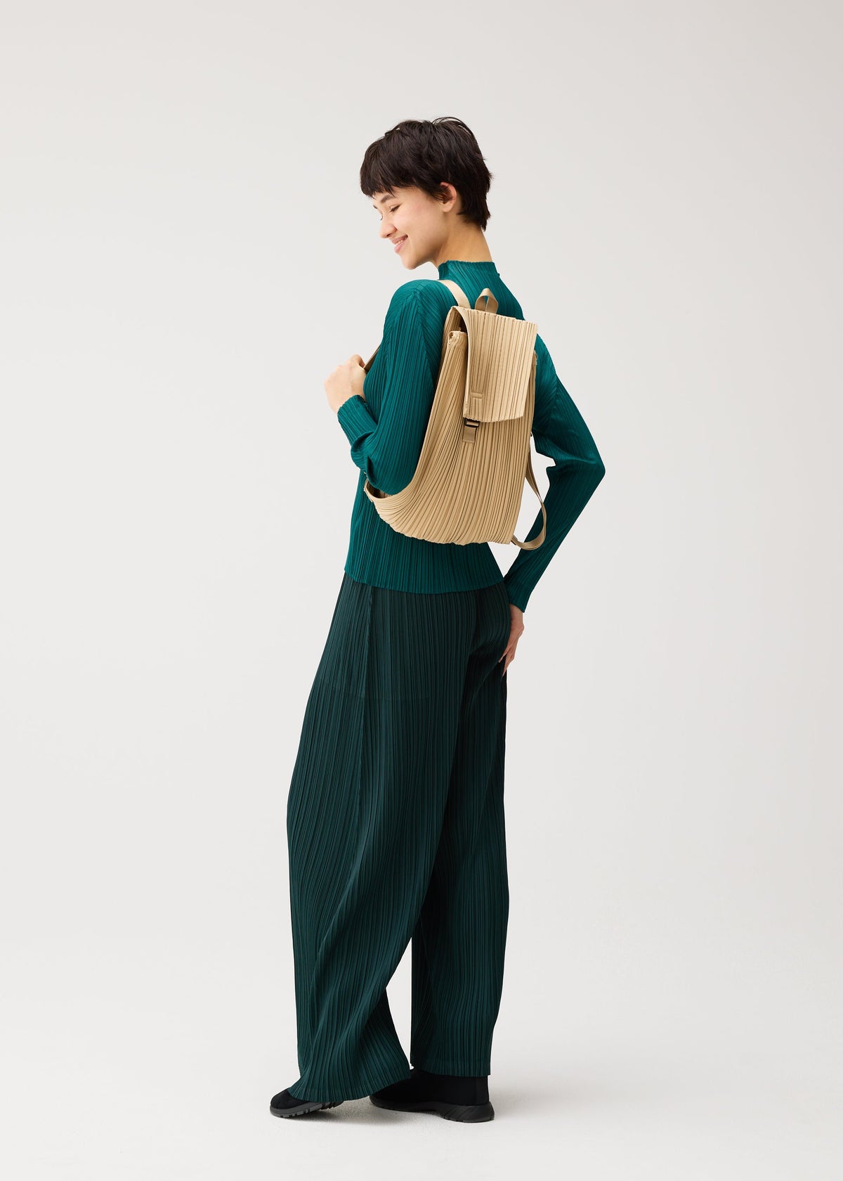 A model wears the PLEATS PLEASE ISSEY MIYAKE PLEATS KNAPSACK pleats-knapsack-backpack-black.